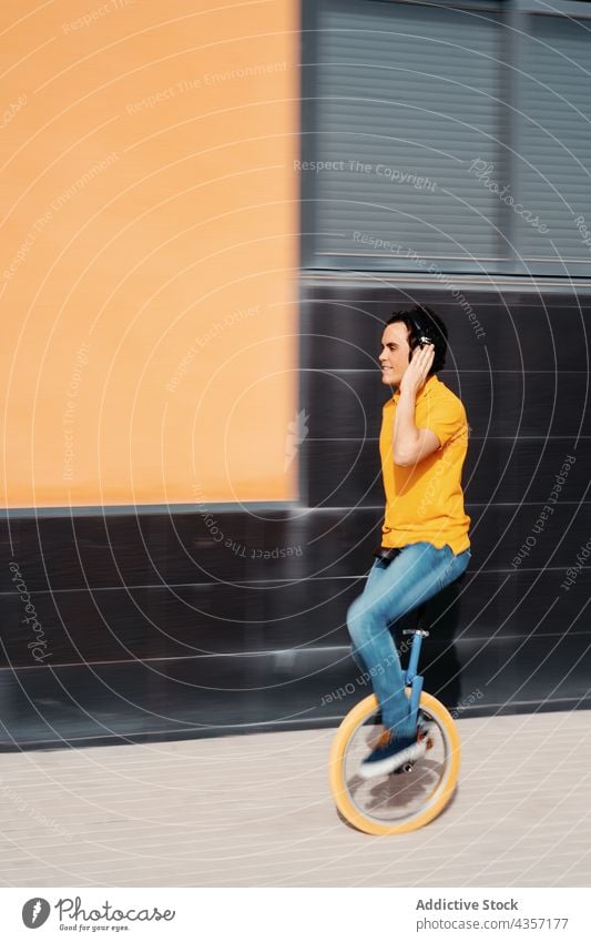 Junger Mann mit Kopfhörern fährt Einrad Mitfahrgelegenheit zuhören urban Farbe modern Apparatur orange männlich Musik Gerät Stil Lifestyle benutzend Rad