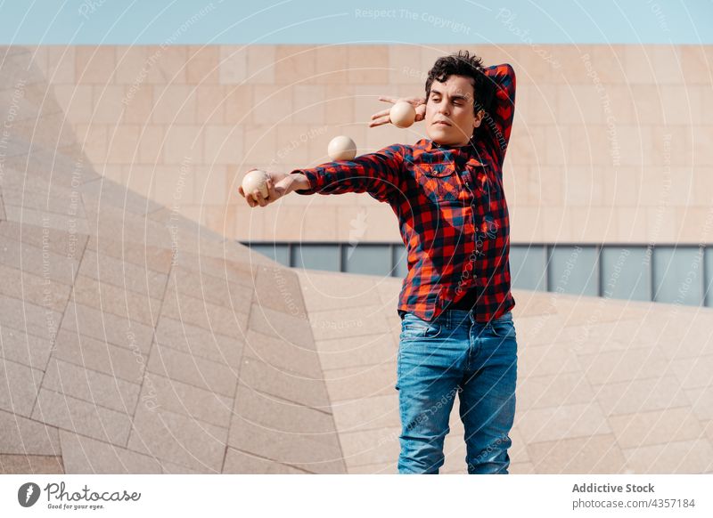 Junger Mann jongliert Bälle in der Nähe eines modernen Gebäudes jonglieren Trick Ball ausführen Architektur Zeitgenosse Geometrie unterhalten Talent Kunst