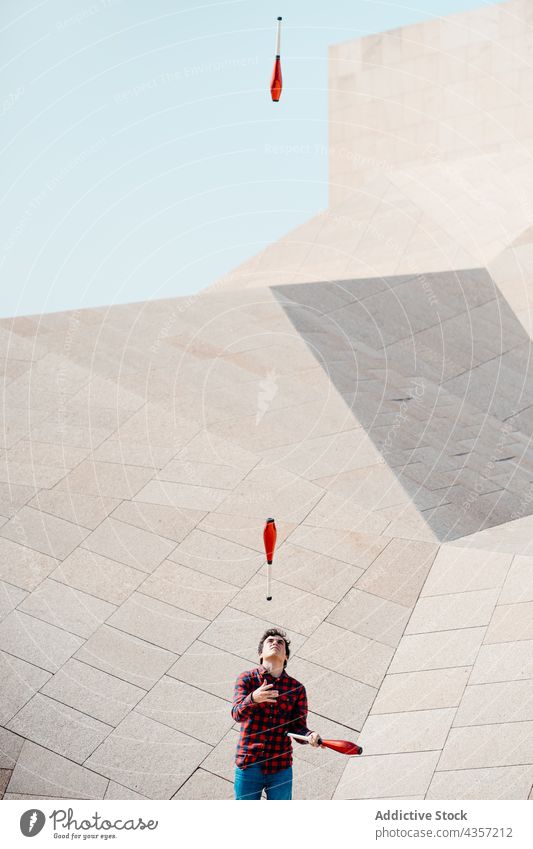Mann jongliert Keulen in der Nähe eines geometrischen Gebäudes jonglieren Club Trick ausführen Architektur Zeitgenosse Geometrie unterhalten Talent Kunst
