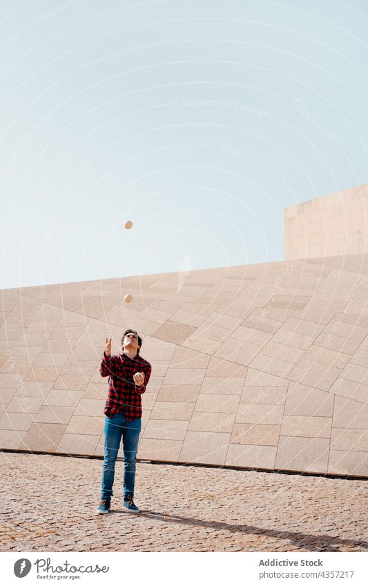 Mann jongliert Keulen in der Nähe eines geometrischen Gebäudes jonglieren Club Trick ausführen Architektur Zeitgenosse Geometrie unterhalten Talent Kunst