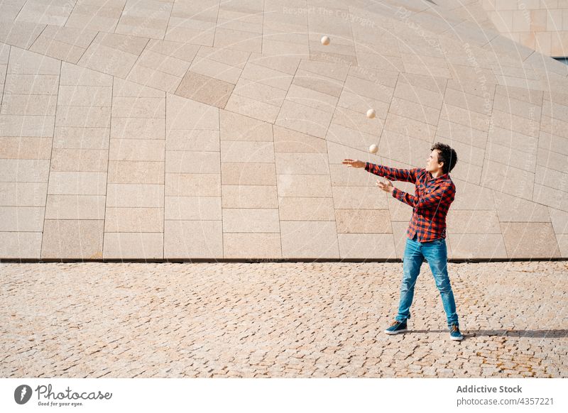 Junger Mann jongliert Bälle in der Nähe eines modernen Gebäudes jonglieren Trick Ball ausführen Architektur Zeitgenosse Geometrie unterhalten Talent Kunst