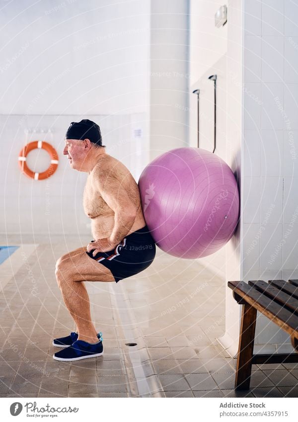 Älterer Mann macht Übungen mit Fitnessball im Pool Aerobic Ball Passform-Ball Training reif Kniebeuge männlich Lebensmitte Wasser aqua Sport Aktivität