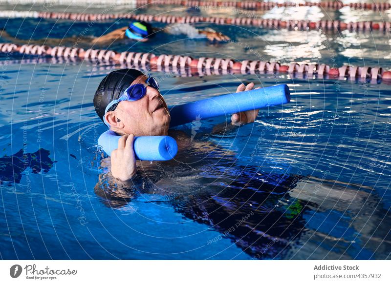 Älterer Mann schwimmt auf einer Wassernudel im Pool schwimmen aqua Nudel Aerobic Übung reif Training männlich Aktivität Sport Badebekleidung Gesundheit