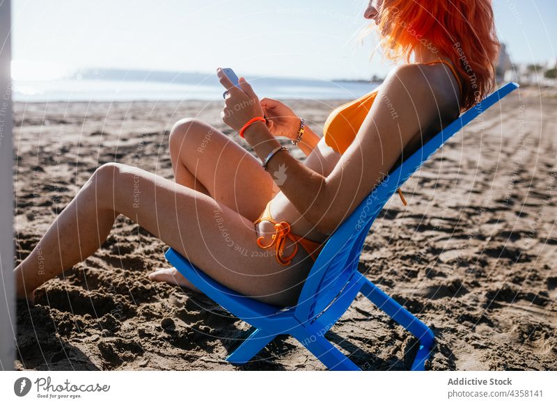 Anonyme Frau mit Telefon am Strand sitzend Bikini benutzend passen Sommer Urlaub MEER reisen Technik & Technologie Browsen Feiertag blass anonym jung Rotschopf