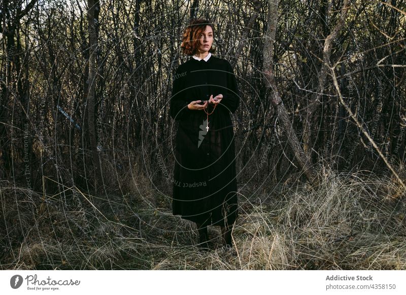 Emotionslose Frau in schwarzem Kleid zu Halloween im Wald stehend anketten durchkreuzen Outfit Mysterium Feiertag Wälder Herbst Phantasie Veranstaltung dunkel