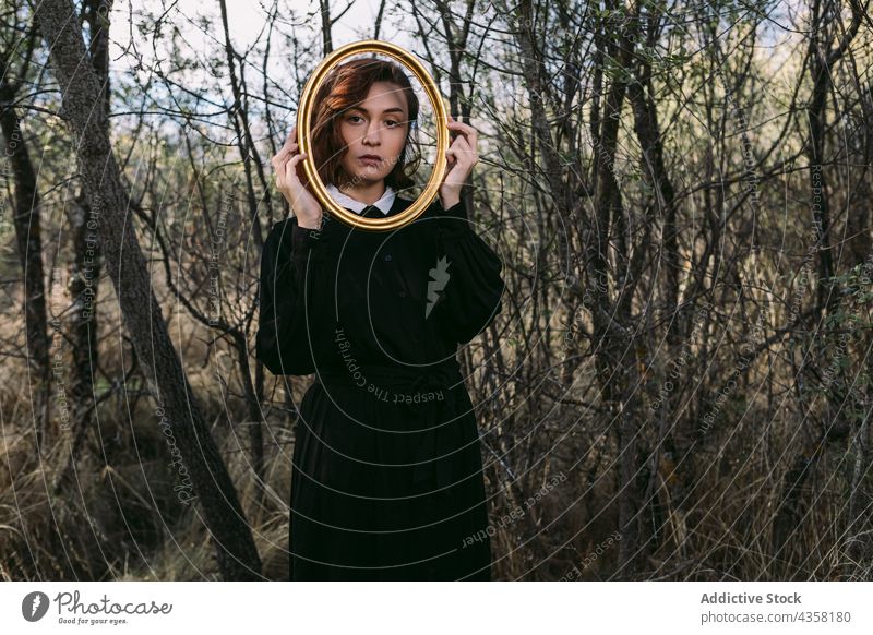 Frau im schwarzen Kleid schaut durch einen Holzrahmen in die Kamera emotionslos Halloween Wald Herbst Feiertag Rahmen hölzern Stil Mysterium Wälder fallen