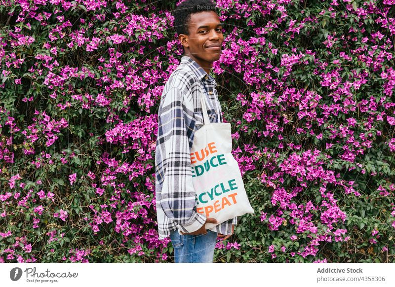 Zufriedener schwarzer Mann mit umweltfreundlichem Stoffbeutel im Garten stehend Tasche Textil Einkaufstasche keine Verschwendung natürlich Ökologie Blume