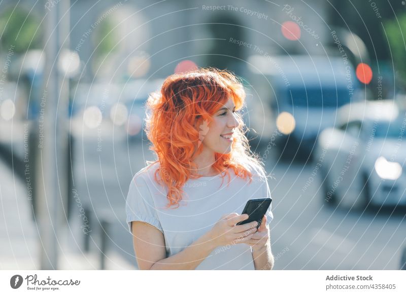 Vergnügte Frau mit roten Haaren, die auf der Straße über Kopfhörer Musik hört Smartphone Browsen Rotschopf Nachricht soziale Netzwerke rote Haare benutzend