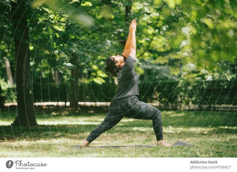 Mollige Frau in Crescent Lunge Pose im Sommer Park Yoga halbmondförmiger Ausfallschritt Gleichgewicht Gesunder Lebensstil Energie Dehnung Arme hochgezogen