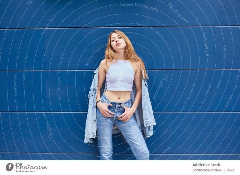 Selbstbewusste stilvolle Frau in Jeans-Outfit steht gegen blaue Wand Stil Jeanshose Jeansstoff Großstadt cool trendy Mode Jacke Straße urban selbstbewusst ernst