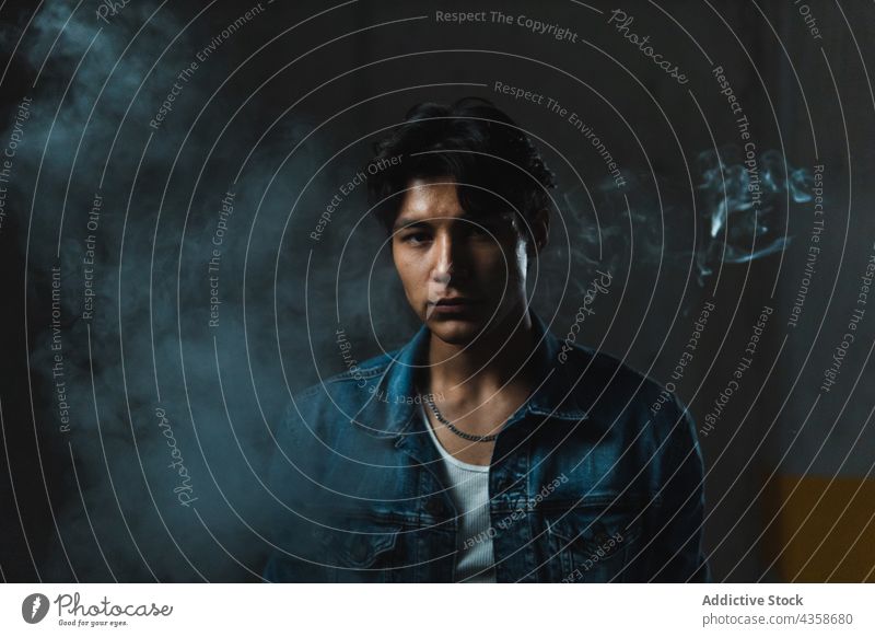 Junger lateinischer Mann Porträt Latein jung selbstbewusst in die Kamera schauen geheimnisvoll Rauch trotzig gutaussehend hispanisch von unten Typ lässig