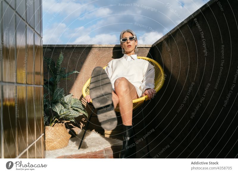Stilvolle Transgender-Frau sitzt im Sessel auf der Terrasse trendy selbstbewusst queer lgbt Mode Outfit sich[Akk] entspannen modern ruhen sitzen Armsessel