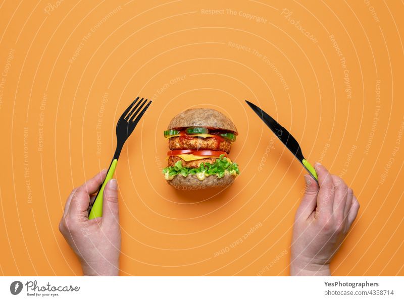 Essen eines veganen Burgers in der Draufsicht auf einem orangefarbenen Hintergrund. oben alternativ Brot Brötchen Käse Cheeseburger Farbe Konsumverhalten Küche