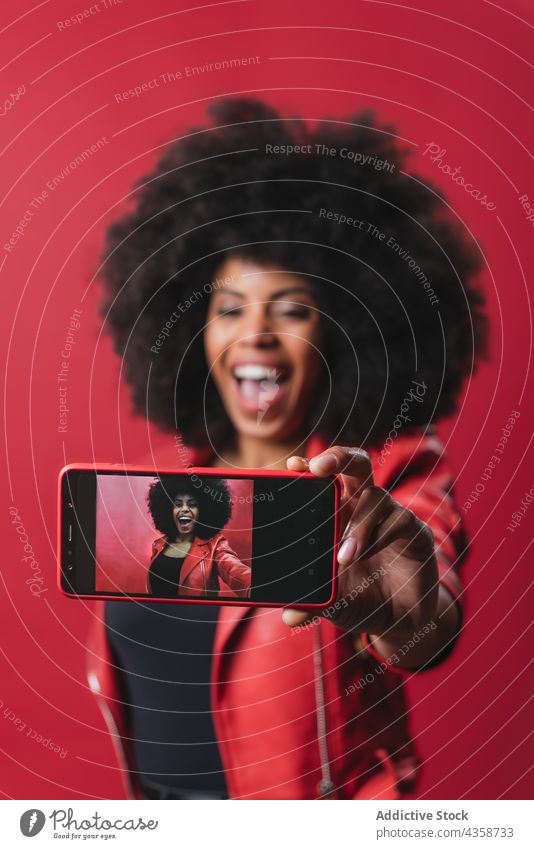 Schwarze Frau macht Selfie mit Smartphone im Studio schwarz Afro-Look Selbstportrait rot Farbe Foto Frisur Gedächtnis Afroamerikaner ethnisch Telefon Gerät