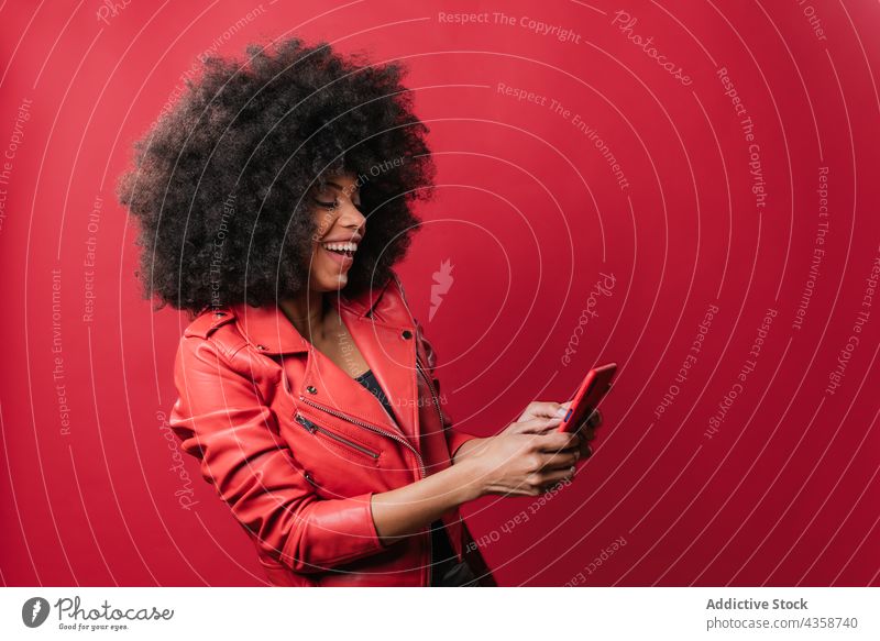 Schwarze Frau beim Surfen auf dem Smartphone im Studio schwarz Afro-Look benutzend aufgeregt Browsen Nachricht rot Farbe hell Afroamerikaner ethnisch Frisur