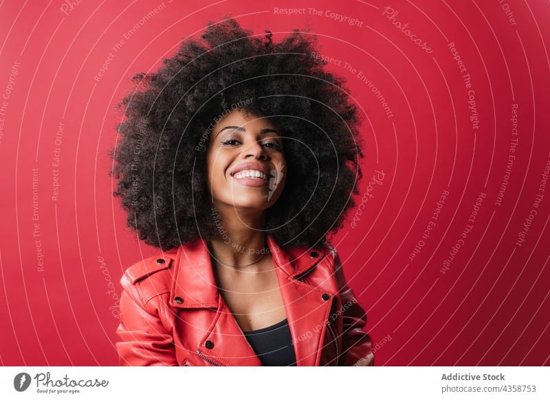 Fröhliche schwarze Frau mit lockigem Haar schaut in die Kamera auf rotem Hintergrund Afro-Look Frisur heiter Vorschein Lächeln Farbe krause Haare charmant