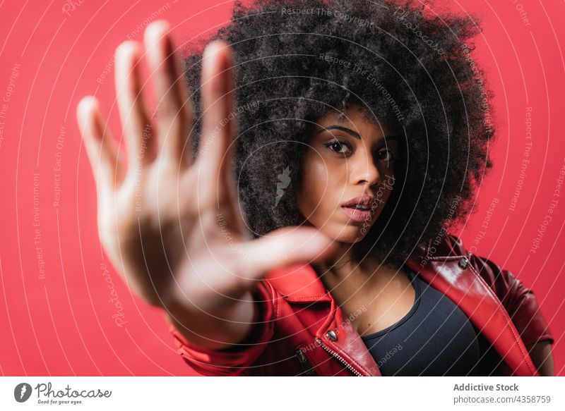 Verängstigte schwarze Frau zeigt Stoppschild auf rotem Hintergrund stoppen gestikulieren Zeichen erschrecken behüten verbieten nein expressiv ablehnen ethnisch