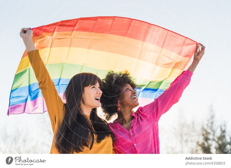 Positive multiethnische lesbische Frauen mit LGBT-Fahne in der Stadt lgbt Homosexualität Regenbogen Stolz gleich Paar Toleranz rassenübergreifend vielfältig