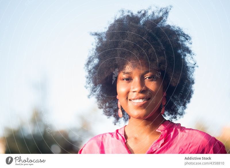 Fröhliche schwarze Frau mit Afrofrisur steht im Park Afro-Look Frisur charmant heiter Lächeln Sommer Schönheit natürlich Afroamerikaner ethnisch sonnig