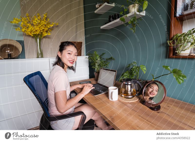 Zufriedene asiatische Frau, die ein Dokument auf ihrem Laptop liest und zu Hause arbeitet freiberuflich Arbeit heimwärts Lächeln lesen Schriftstück Computer