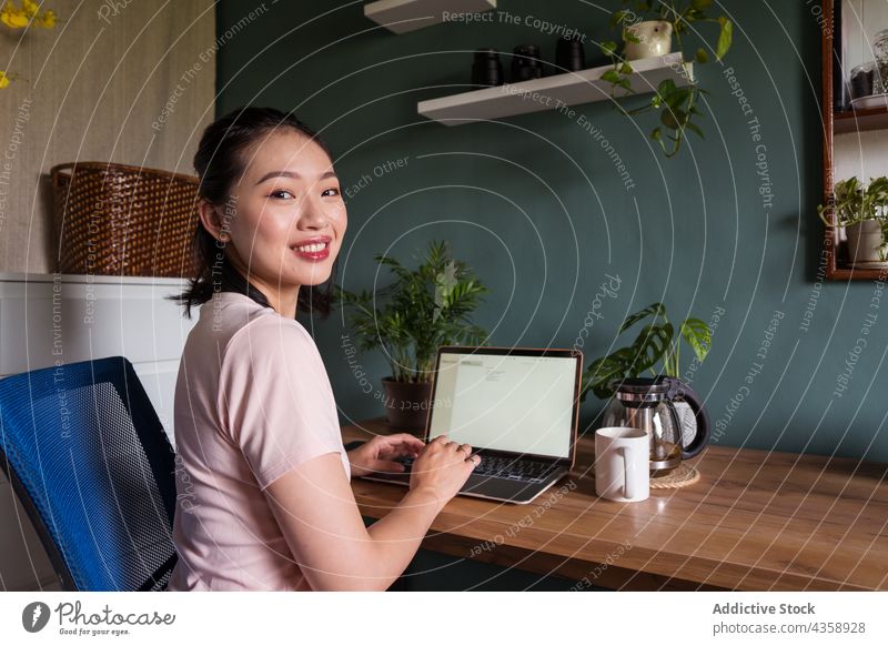 Zufriedene asiatische Frau, die ein Dokument auf ihrem Laptop liest und zu Hause arbeitet freiberuflich Arbeit heimwärts Lächeln lesen Schriftstück Computer