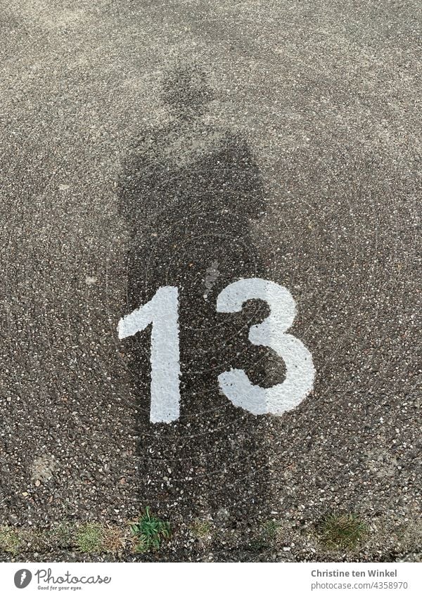 Die Zahl 13 in weißer Farbe auf grobem grauem Asphalt und der Schatten der Fotografin I gezeichnet & gemalt Dreizehn Strasse Parkplatz Ziffern & Zahlen