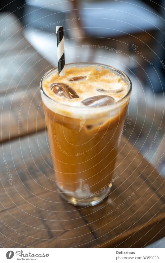 Seitenansicht eines Eis-Latte-Kaffees mit Strohhalm auf einem Holztisch Kaffee-Latte melken kalt trinken Eiswürfel Café Kantine Koffein Nahaufnahme Hintergrund