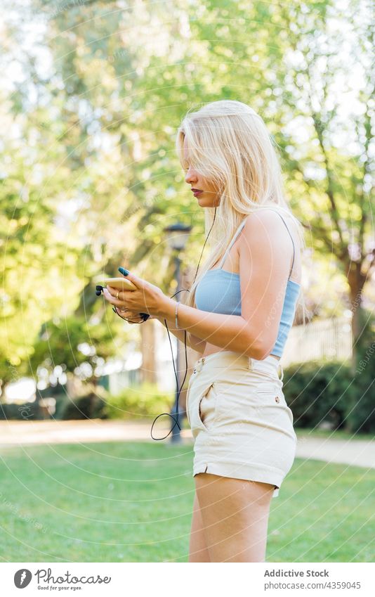 Frau hört Musik mit Kopfhörern im Park zuhören Sommer Gesang Smartphone unterhalten Gelassenheit genießen Melodie Apparatur Gerät Audio sorgenfrei Klang