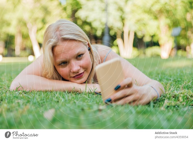 Glückliche Frau, die ein Selfie macht und Musik auf grünem Rasen im Park hört zuhören Kopfhörer Sommer unterhalten Gesang Lächeln genießen Lügen Gras