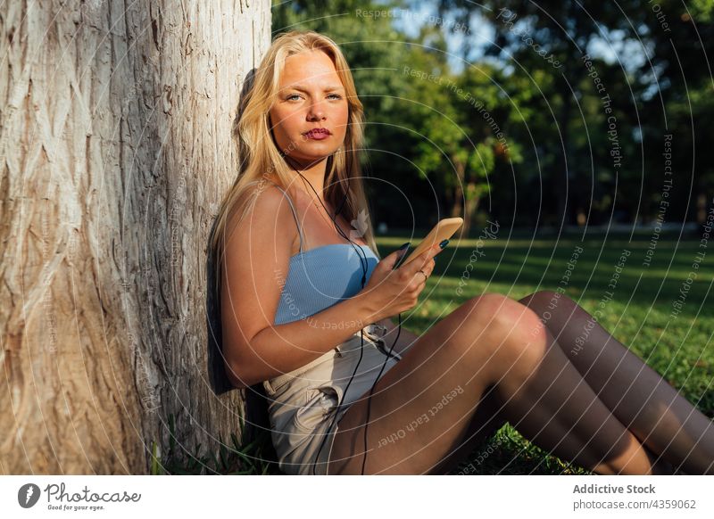 Frau, die im Sommer im Park mit ihrem Mobiltelefon Musik hört zuhören Smartphone Sonnenuntergang Gesang genießen sorgenfrei benutzend Mobile Gerät Kopfhörer