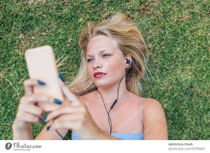 Unbekümmerte Frau, die auf einer Wiese Musik hört zuhören verträumt Kopfhörer Lügen Gras Gesang genießen Park sich[Akk] entspannen Harmonie Sommer ruhen Audio