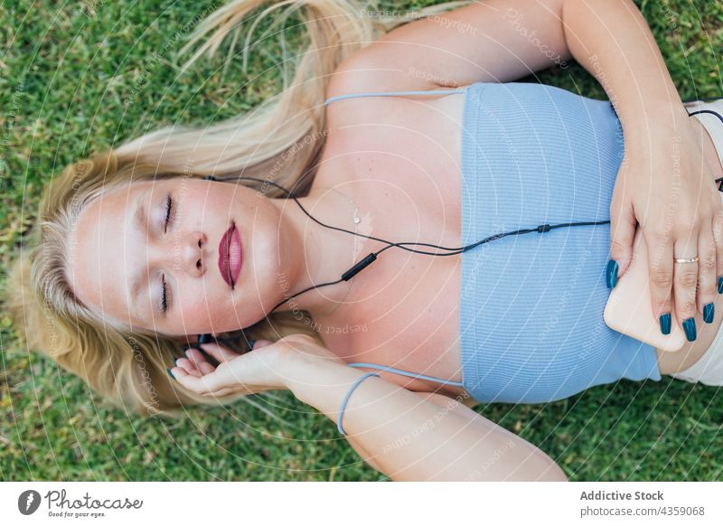 Unbekümmerte Frau hört mit geschlossenen Augen auf einer Wiese Musik zuhören sorgenfrei verträumt Augen geschlossen Kopfhörer Lügen Gras Gesang genießen Park