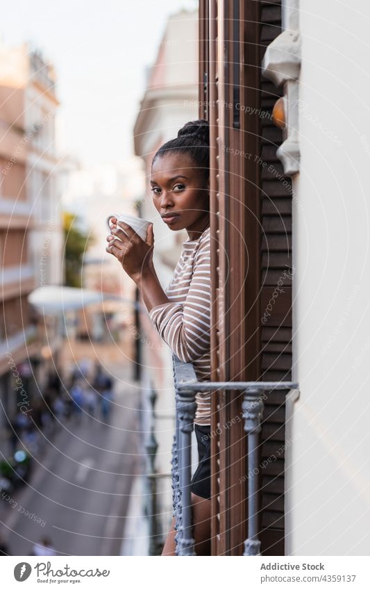 Schwarze Frau mit Kaffee, die vom Balkon aus auf die Stadt blickt reflektierend wehmütig Heißgetränk nachdenklich einsam Haus nachdenken allein Afroamerikaner