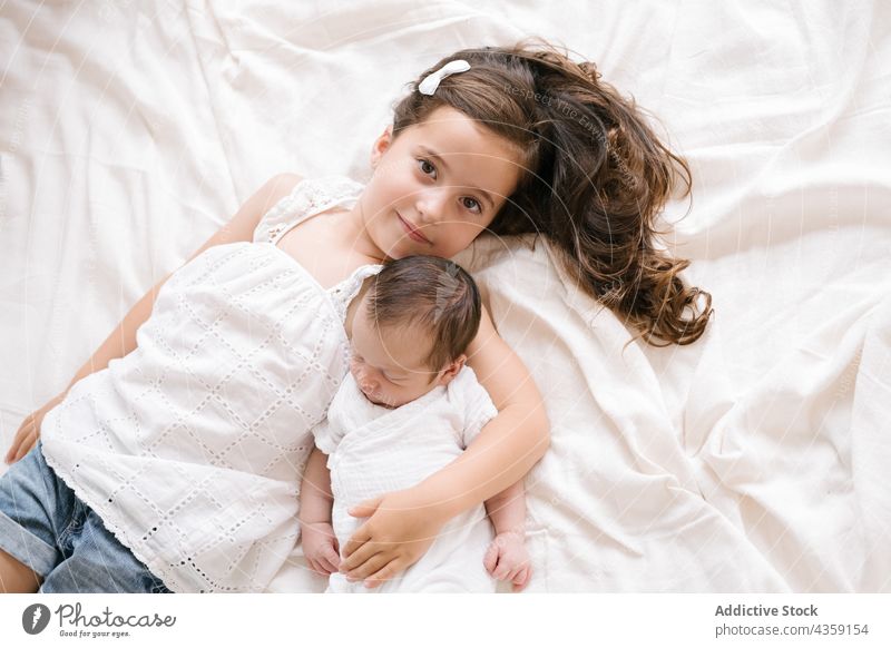 Lächelndes Mädchen mit Neugeborenem auf dem Bett liegend Kind neugeboren Zusammensein Geschwisterkind Lügen Baby Säugling Umarmung niedlich bezaubernd Kindheit