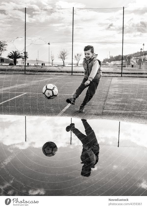 Junge kickt einen Ball auf schwarz-weiß Kind 1 jung Jugend Fußball im Freien außerhalb Park Straßenbelag schwarz auf weiß Bein rund Sport aktiv Lifestyle