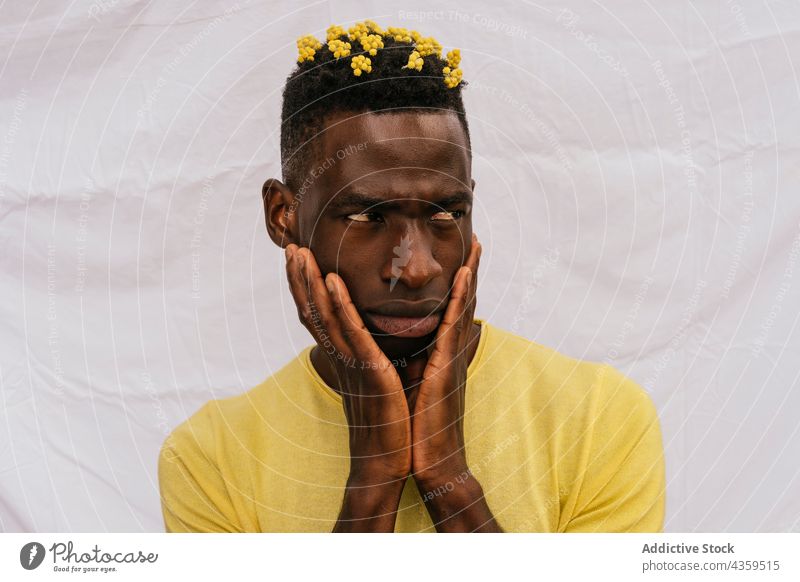 Ernster schwarzer Mann mit gelben Blumen im Haar Behaarung Wildblume Farbe ernst Stirnrunzeln trendy Blütezeit männlich ethnisch Afroamerikaner Stil Model