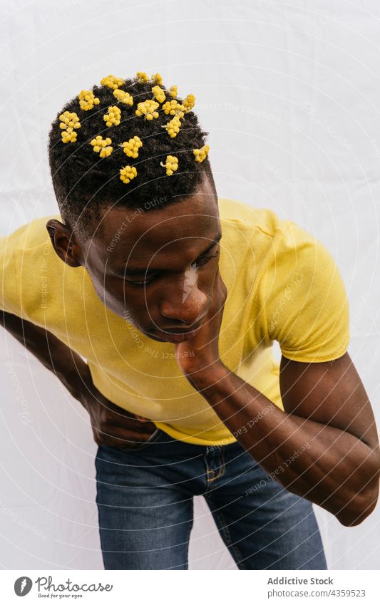 Ernster schwarzer Mann mit gelben Blumen im Haar Behaarung Wildblume Farbe ernst trendy Blütezeit männlich ethnisch emotionslos Afroamerikaner Stil Model