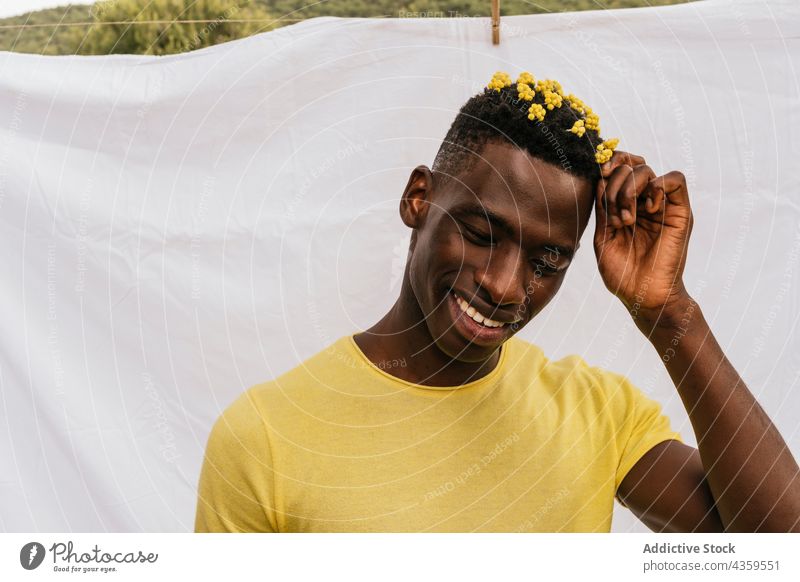 Glücklicher schwarzer Mann mit gelben Blumen im Haar Behaarung Wildblume Farbe trendy Blütezeit männlich ethnisch Afroamerikaner Stil Model Vorschein