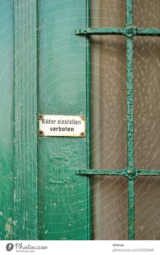 An einer alten, grün gestrichenen Haustür mit Glasteil ist ein kleines weißes Schild mit der Aufschrift - Räder einstellen verboten - befestigt / wohnen / Nostalgie