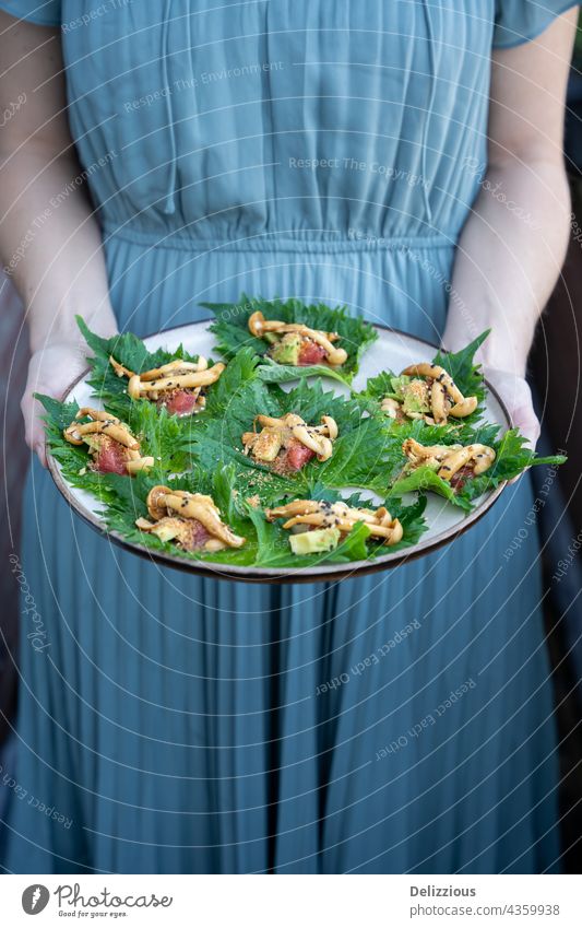 Eine Frau in einem blauen Kleid hält einen Teller mit veganen asiatischen Vorspeisen Amuse-Gueule Hände Waffen Lebensmittel Veganer Vegetarier Beteiligung