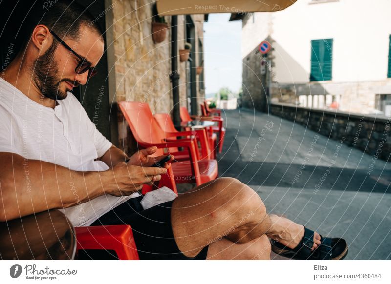 Mann sitzt im Urlaub in einem italienischen Straßencafé und guckt auf sein Handy Café Italien Sommer Tourist Altstadt Tourismus Ferien & Urlaub & Reisen