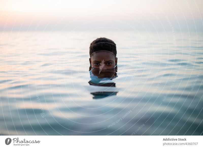 Schwarze Frau mit kurzen Haaren und halbem Gesicht im Meer MEER Wasser Hälfte Sonnenuntergang Rippeln Abend Sommer ethnisch schwarz Afroamerikaner ruhig