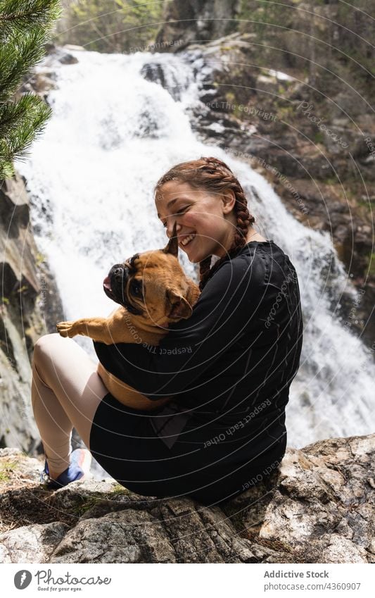 Fröhliche reisende Frau mit Hund in der Nähe eines Wasserfalls im Wald Reisender Tier Wanderer Zusammensein Pyrenäen französische Bulldogge Begleiter Glück
