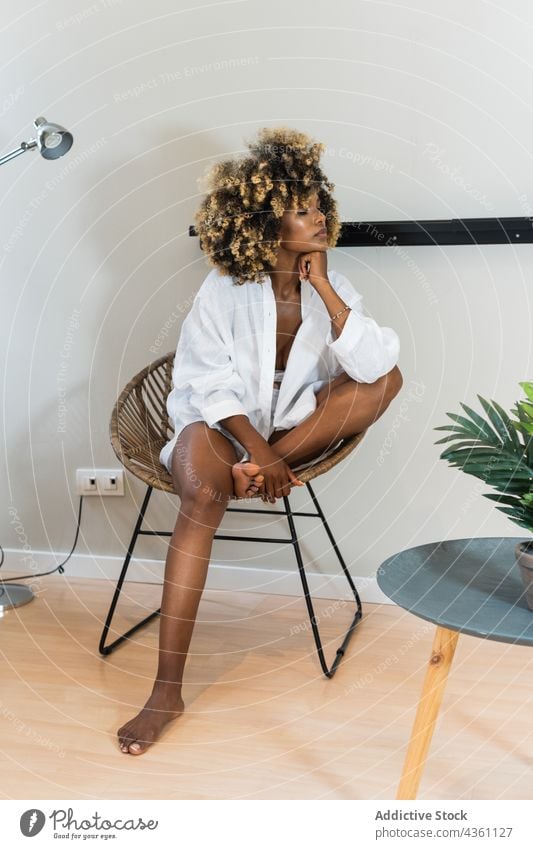 Schwarze Frau sitzt auf einem runden Stuhl in einem hellen Raum Denken ruhig Sorge nachdenken Appartement sich auf die Hand lehnen Melancholie zu Hause