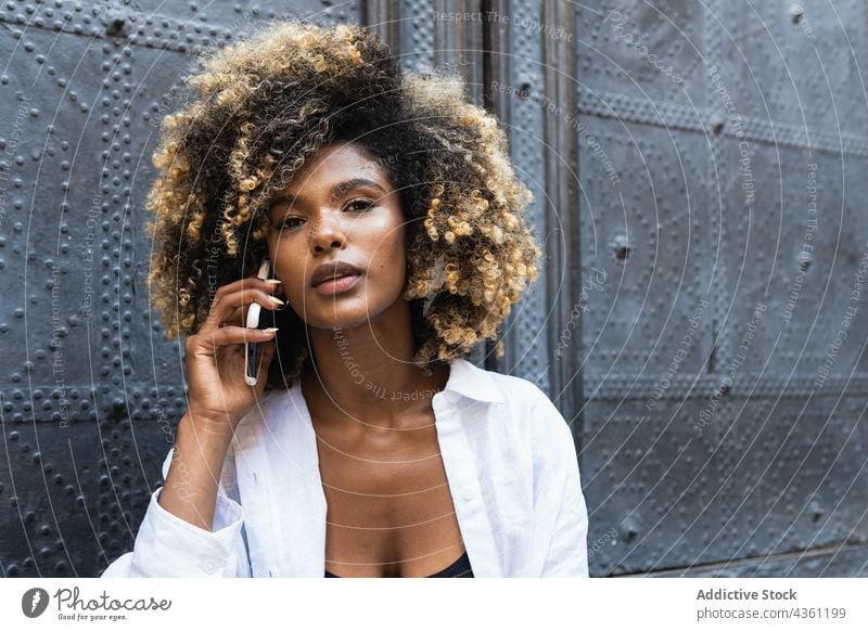 Junge schwarze Frau spricht mit ihrem Smartphone, während sie in der Nähe eines Gebäudes sitzt Telefonanruf sprechen benutzend Kommunizieren Gespräch Apparatur
