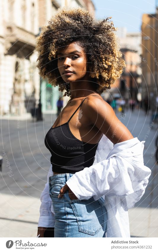 Schwarze Frau steht auf der Straße und schaut in die Kamera ernst urban tausendjährig Körperhaltung schön Gebäude lässig attraktiv brünett lange Haare Frisur