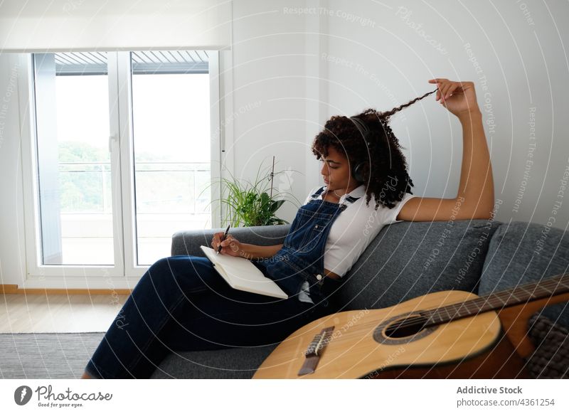 Schwarzer Musiker komponiert Musik zu Hause Frau komponieren nachdenklich zuhören Kopfhörer Notebook heimwärts besinnlich kreativ Notizblock ethnisch schwarz