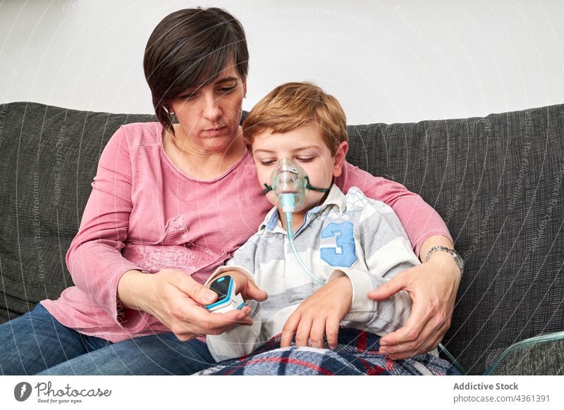 Mutter mit Pulsoxymeter am Finger des Kindes in der Sauerstoffmaske messen Zusammensein Mundschutz inhalieren Verfahren krank heimwärts medizinisch geduldig