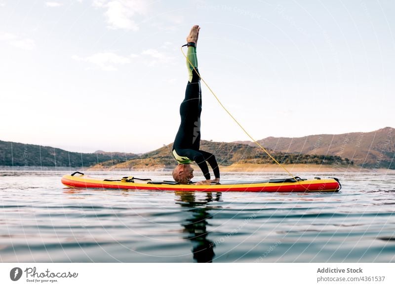 Mann macht Yoga auf Paddleboard im Meer Paddelbrett Zusatzplatine Kopfstand Pose üben Gleichgewicht Asana MEER männlich Surfer Sonnenuntergang Surfbrett