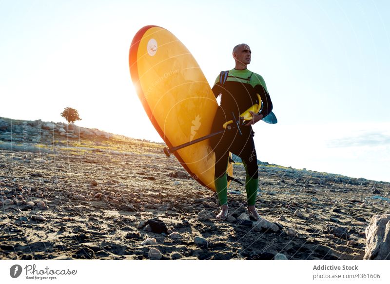 Sportlicher Mann mit Paddelbrett am Strand stehend Holzplatte selbstbewusst Aktivität üben Training Herausforderung männlich aktiv sportlich Lebensmitte reif